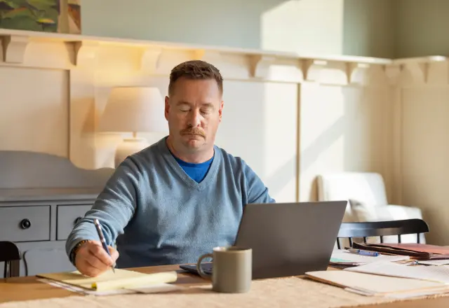 middle-aged male subject taking notes in front of a laptop